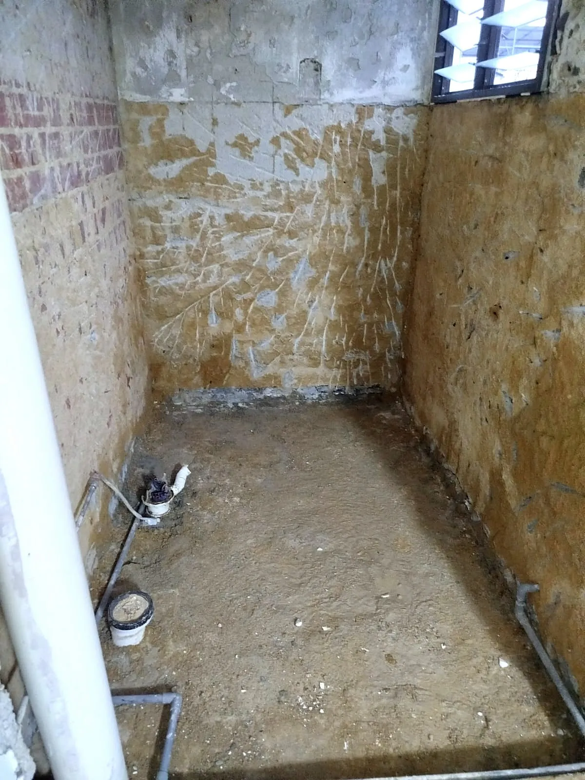 A bathroom hacked back to the original screed and brickwork, with drainage and pipework exposed