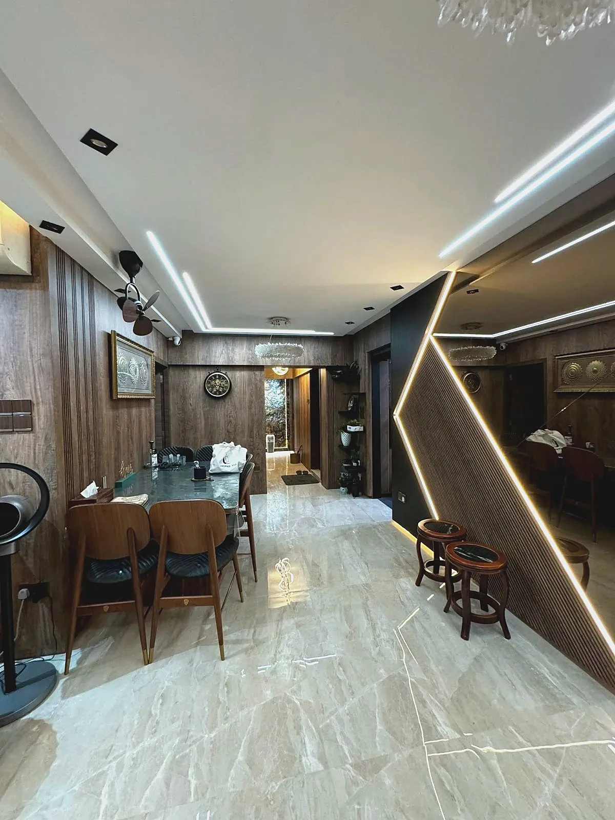 A dining area finished in dark timber panelling with recessed linear lighting, a fluted feature wall lit along its edge, and polished marble-effect floor tiles