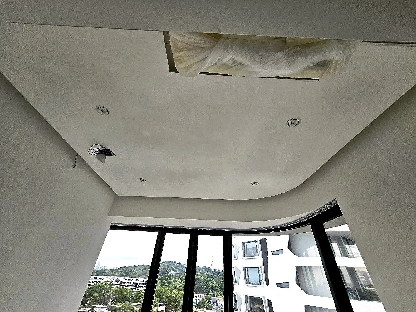 A curved false ceiling under construction above a bay window, with downlight cut-outs set out and an access hatch left open