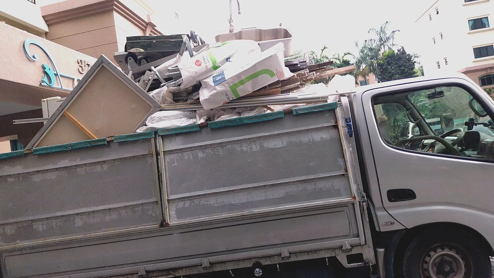 A lorry at a building entrance loaded with stripped-out partitions, a sink, cement bags and metal framing for disposal