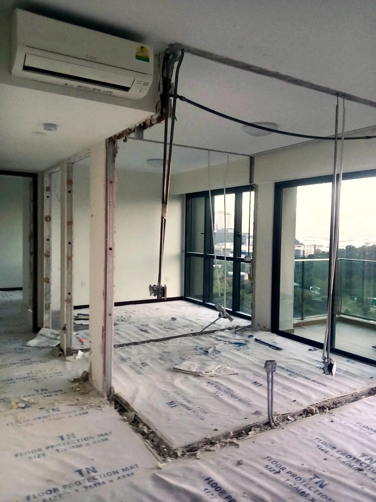 An office unit mid strip-out: a partition removed back to the slab, steel props holding the ceiling, and floor protection laid wall to wall in front of the glazed facade